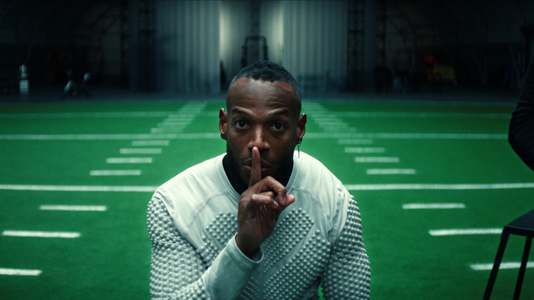 Isaiah White holds a finger to his lips on a football field in Him
