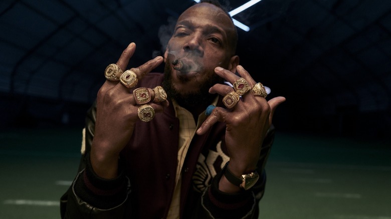 Isaiah White flashing his eight championship rings while smoking a cigar in Him