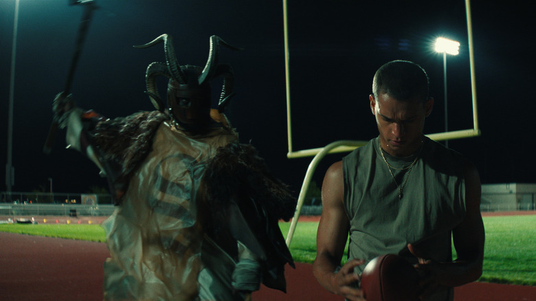 A man dressed as a horned devil raises a hammer to attack Cam Cade in HIM