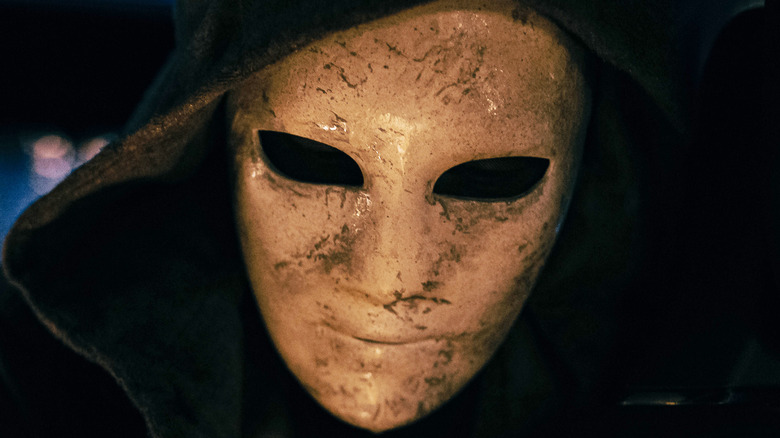 A hooded figure wearing a mask is seen in closeup in Dark Matter