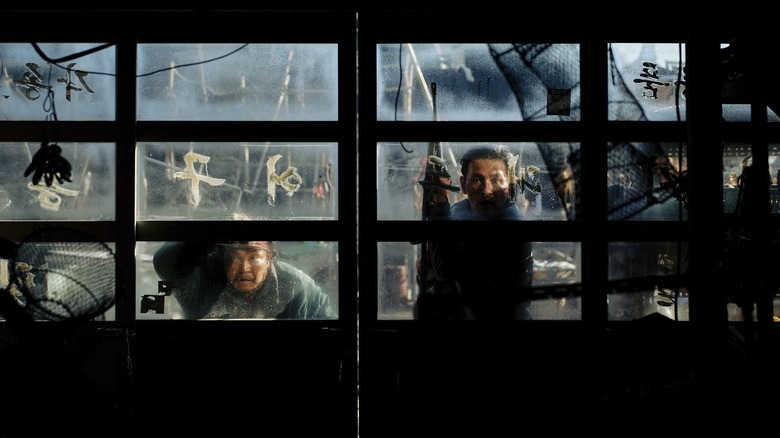 Hwang Jung-min as Bum-seok holding a weapon and staring through a garage window in Hope