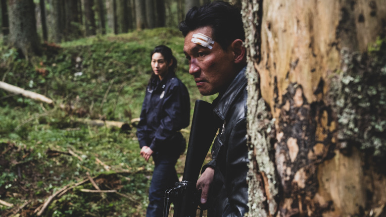 Hwang Jung-min as Bum-seok standing in a forest with a bandage on his head next to Hoyeon as Sung-ae in Hope