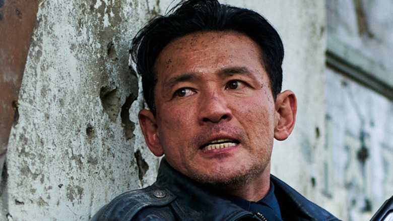 Hwang Jung-min as Bum-seok leaning against a destroyed building in Hope