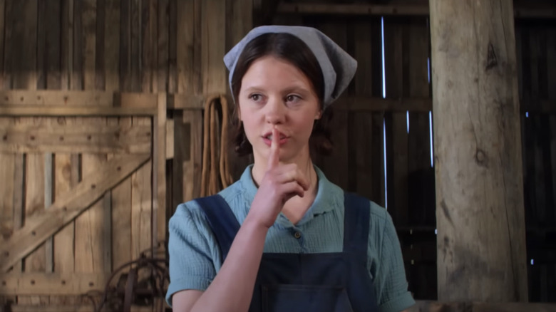 Mia Goth putting finger to her lips in barn in Pearl