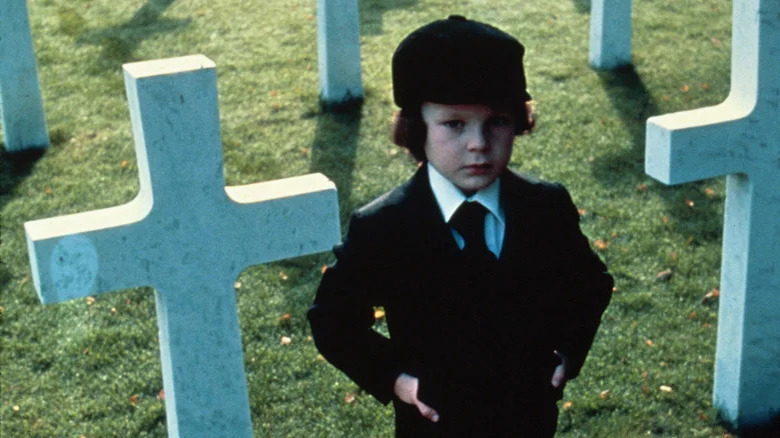 Small child in suit standing in graveyard in The Omen