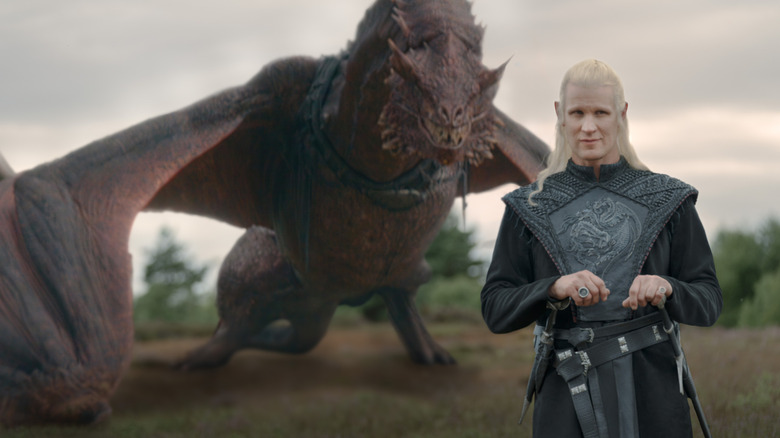 Matt Smith as Daemon Targaryen standing in full armor on an empty field with a dragon at his back in House of the Dragon