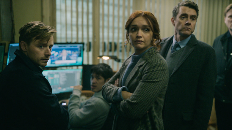 Olivia Cooke as Sid Baker standing in a room with her arms crossed next to Jack Lowden as River Cartwright, Christopher Chung as Roddy Ho, and Paul Higgins as Struan Loy in Slow Horses