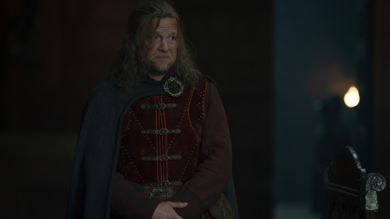 Tom Bennett  as Ulf the White wearing a cape and fine clothes and standing with his hands folded in House of the Dragon