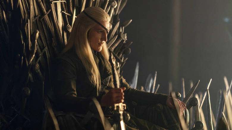 Ewan Mitchell as Aemond Targaryen sitting on the Iron Throne with a sword in hand in House of the Dragon Season 3