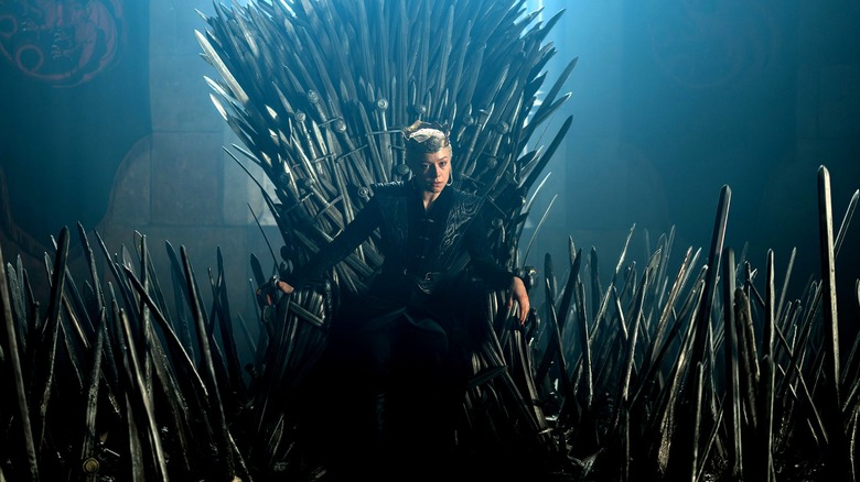 Emma D'Arcy as Rhaenyra Targaryen seated on a throne and surrounded by several swords embedded in the ground in House of the Dragon