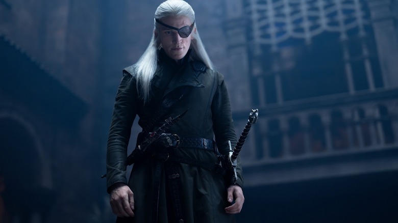 Ewan Mitchell as Aemond Targaryen wearing an eye patch and standing over someone threateningly in House of the Dragon