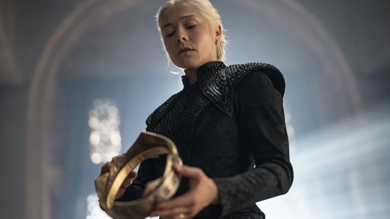 Emma D'Arcy as Rhaenyra Targaryen dressed in black and holding up a crown in House of the Dragon