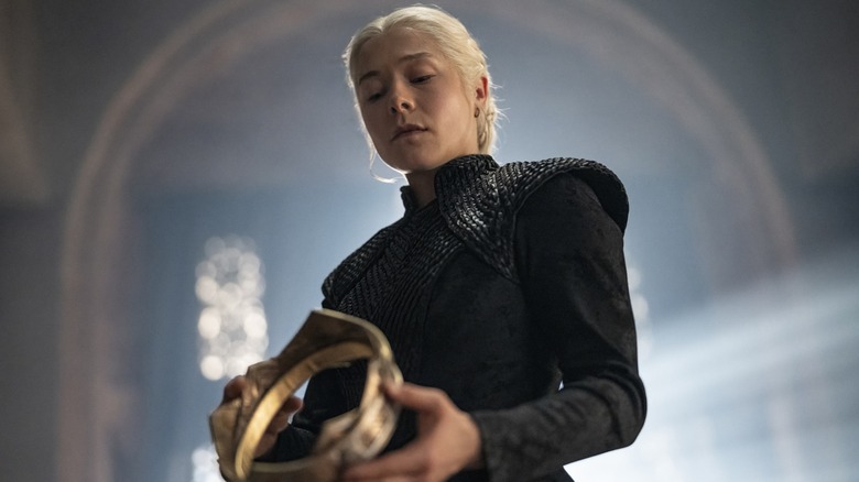 Emma D'Arcy as Rhaenyra Targaryen dressed in black and looking down at the crown in her hands in House of the Dragon