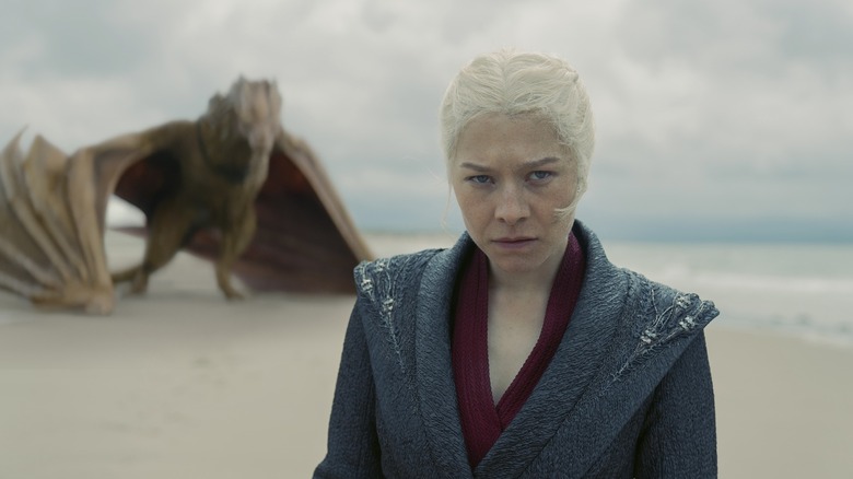 Rhaenyra Targaryen standing on a beach with Syrax hunched in the background in House of the Dragon