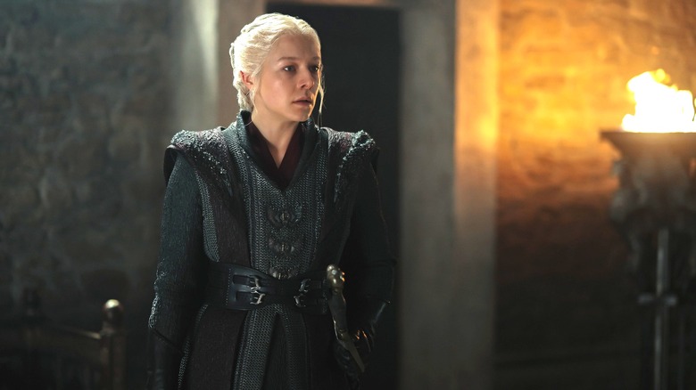 Queen Rhaenyra Targaryen standing in a firelit room alone in A Knight of the Seven Kingdoms