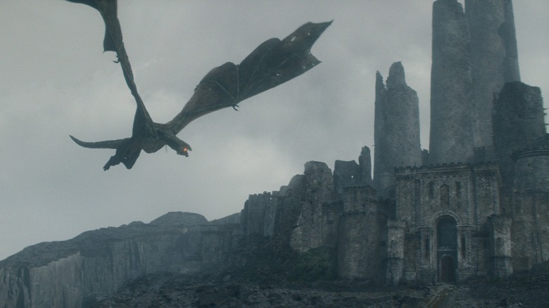 A massive dragon flying over the ruins of an old castle and preparing to breathe fire in House of the Dragon