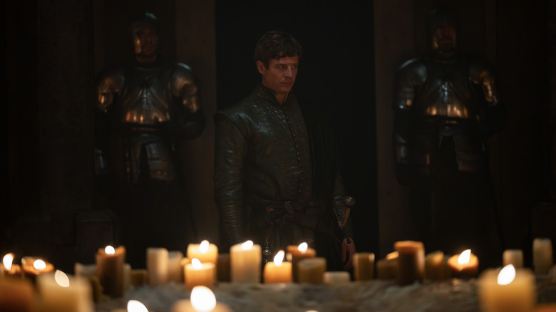 James Norton as Ormund Hightower standing between two armored soldiers with several candles in the foreground in House of the Dragon
