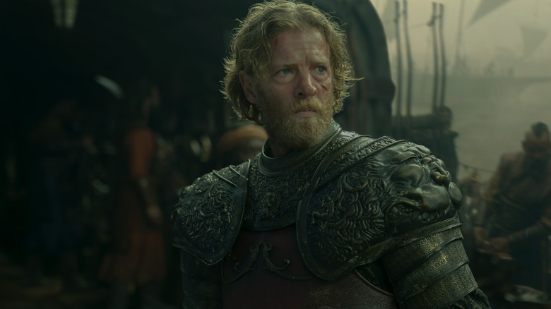 Jefferson Hall as Tyland Lannister wearing heavy armor and looking ragged while standing on a ship surrounded by sailors in House of the Dragon