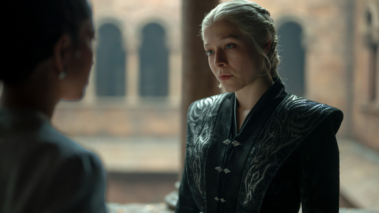 Emma D'Arcy as Rhaenyra Targaryen standing in a courtyard talking to Sonoya Mizuno as Mysaria in House of the Dragon