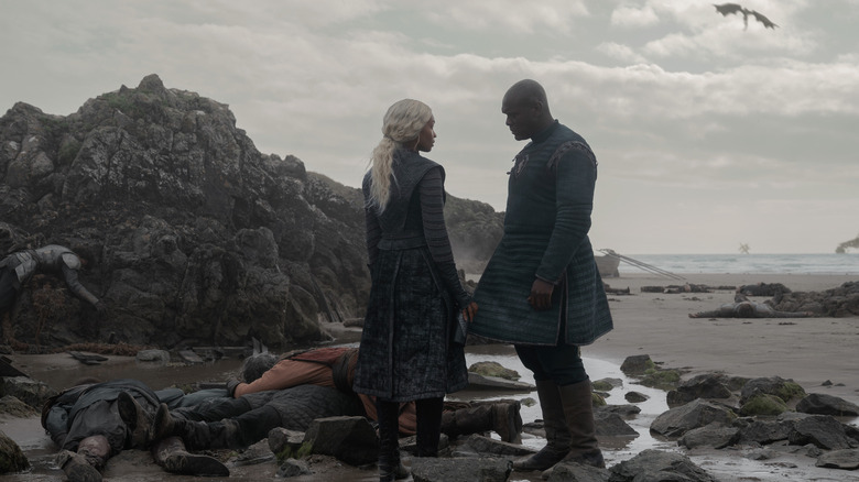 Bethany Antonia as Baela Targaryen standing on a beach next to Abubakar Salim as Alyn of Hull with a dragon flying overhead in House of the Dragon