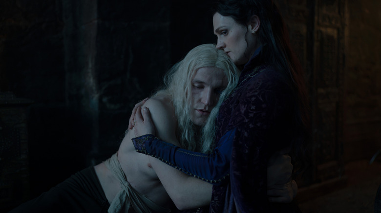 Ewan Mitchell as Aemond Targaryen embracing Gayle Rankin as Alys Rivers in a darkly-lit room in House of the Dragon