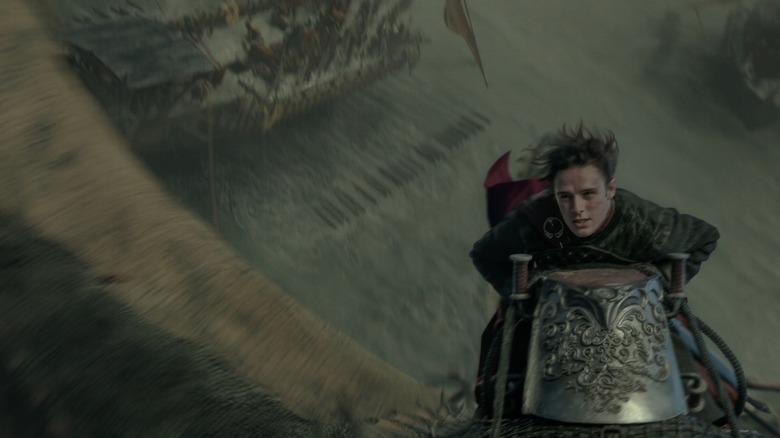 Harry Collett as Jacaerys Velaryon flying a dragon over an ocean filled with warships in House of the Dragon