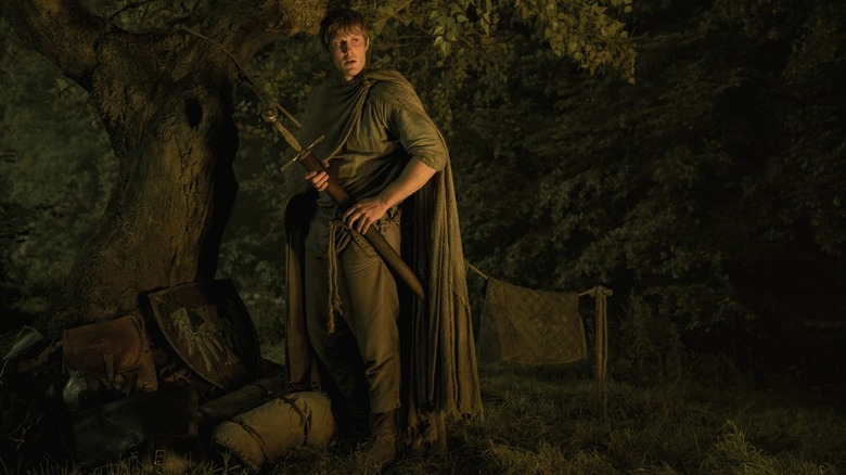 Peter Claffey as Ser Duncan the Tall holding his sword and scabbard and standing by a tree in A Knight of the Seven Kingdoms