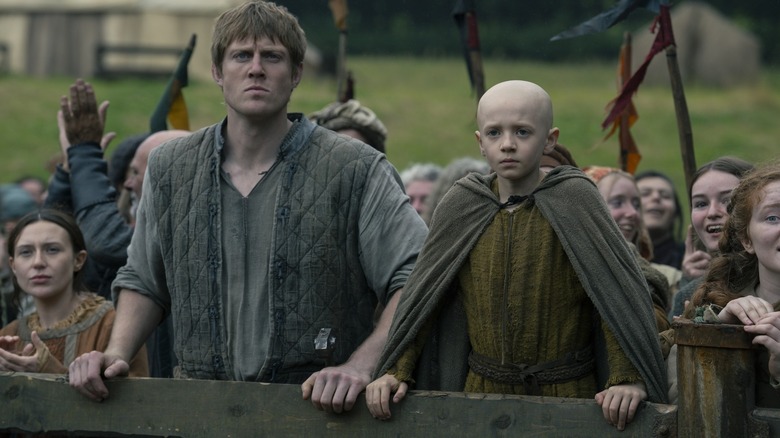 Peter Claffey as Ser Duncan the Tall and Dexter Sol Ansell as Egg standing against a railing amid a large crowd at a joust in A Knight of the Seven Kingdoms