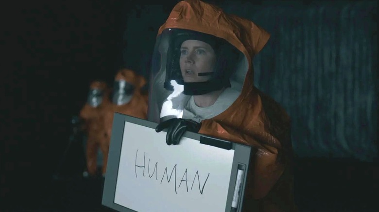 Louise Banks in a space suit, holding a sign that says 