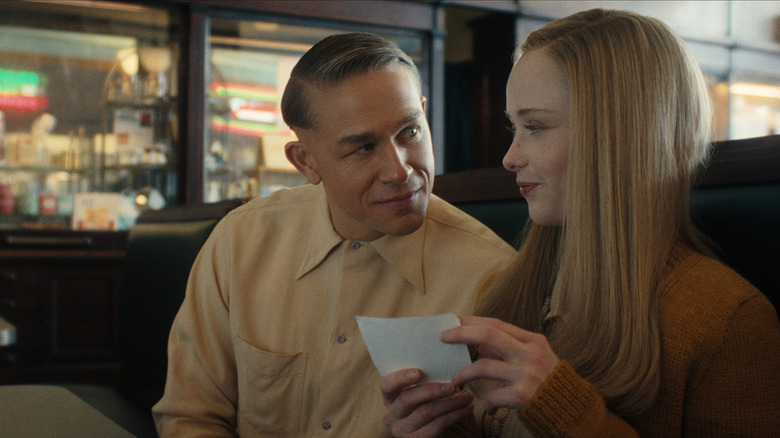 Charlie Hunnam as Ed Gein seated next to Suzanna Son as Adelina in a diner booth in Monster: The Ed Gein Story