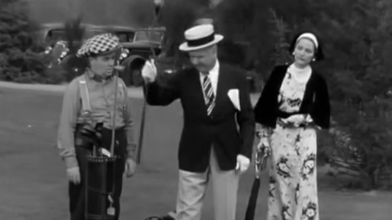 Sam Bisbee holding a golf club in front of his caddy and a young woman in You're Telling Me!