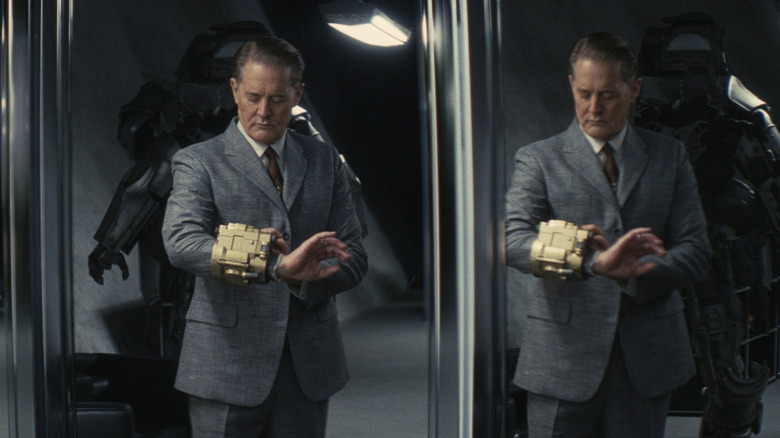 Hank wearing a huge wrist machine looking in a multipaneled mirror on Fallout