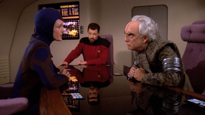 Lorin and Mauric glaring at each other over a table with Riker looking on on Star Trek: The Next Generation