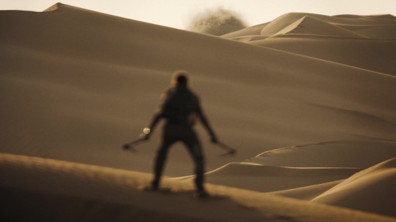Timothée Chalamet's Paul Atreides stands atop a sand dune with hooks drawn as he awaits the arrival of a sandworm in Dune: Part Two