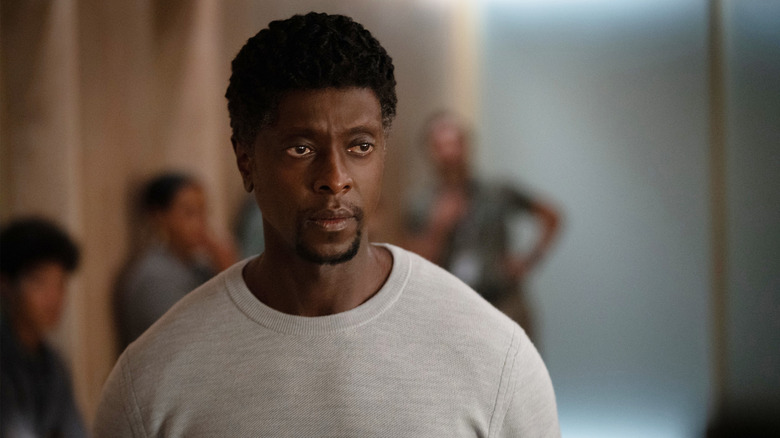 Edi Gathegi as Dev Ayesa standing in a crowded room with a concerned expression on his face in For All Mankind
