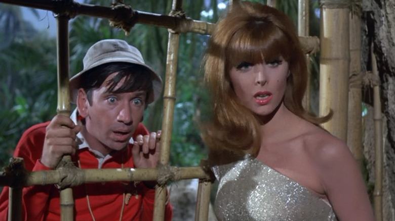 Gilligan and Ginger on opposite sides of a bamboo cage looking shocked on Gilligan's Island