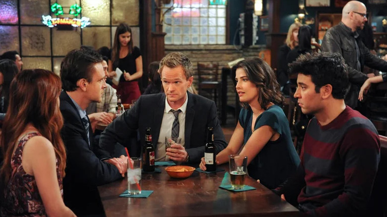 Alyson Hannigan as Lily Aldrin, Jason Segel as Marshall Eriksen, Neil Patrick Harris as Barney Stinson, Cobie Smulders as Robin Scherbatsky, and Josh Radnor as Ted Mosby sitting at a table on How I Met Your Mother
