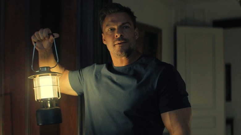 Reacher holds up a lantern inside the Beck mansion in Season 3 of Reacher