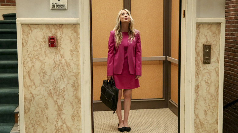 Penny in the elevator looking up in a pink suit in The Big Bang Theory