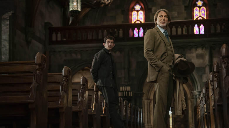 Benoit Blanc en pater Jud staan in een kerk en kijken buiten de camera in Wake Up Dead Man