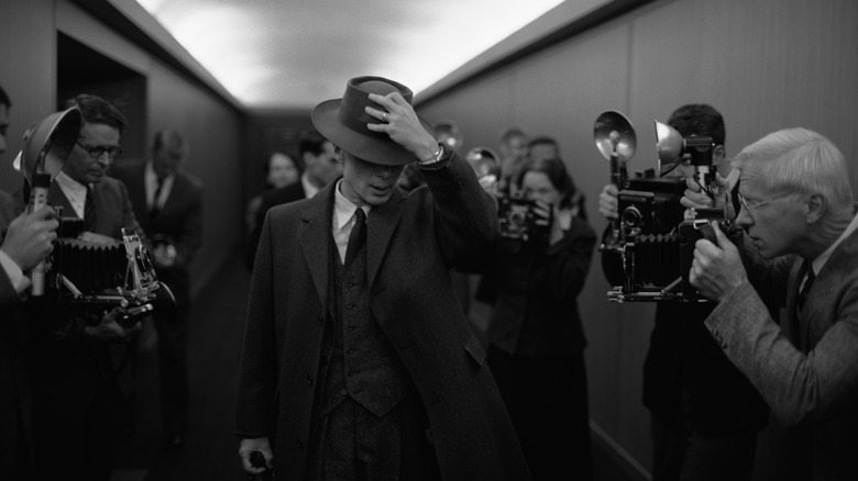 Oppenheimer walking through a crowd of reporters in Oppenheimer