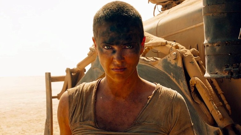 Charlize Theron as Furiosa standing next to her War Rig in Mad Max: Fury Road