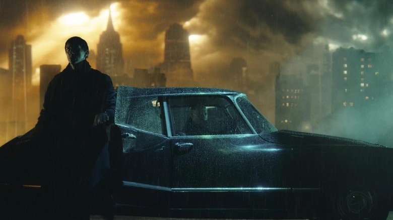 Adam Driver as Cesar leaning on a car standing in the rain in Megalopolis