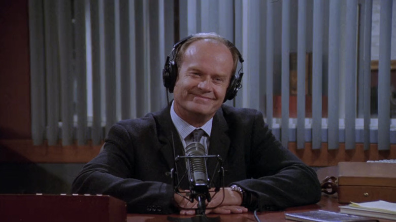 Kelsey Grammer's Frasier Crane smiles as he sits at his radio studio desk in Frasier