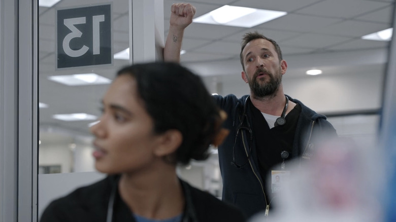 Noah Wyle's Dr. Michael Robinavitch stands in the doorway of an exam room with Supriya Ganesh's Dr. Samira Mohan in the foreground in The Pitt