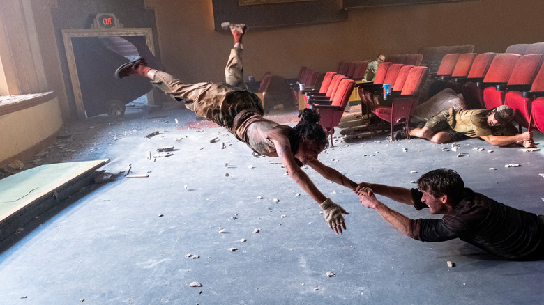 Glen Powell as Tyler holding onto Sasha Lane as Lily as a tornado sucks her out of a destroyed movie theater in Twisters