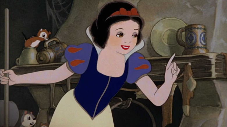 Snow White holds a broom and raises her pointer finger while speaking inside the dusty, cluttered dwarf cottage in Snow White and the Seven Dwarfs