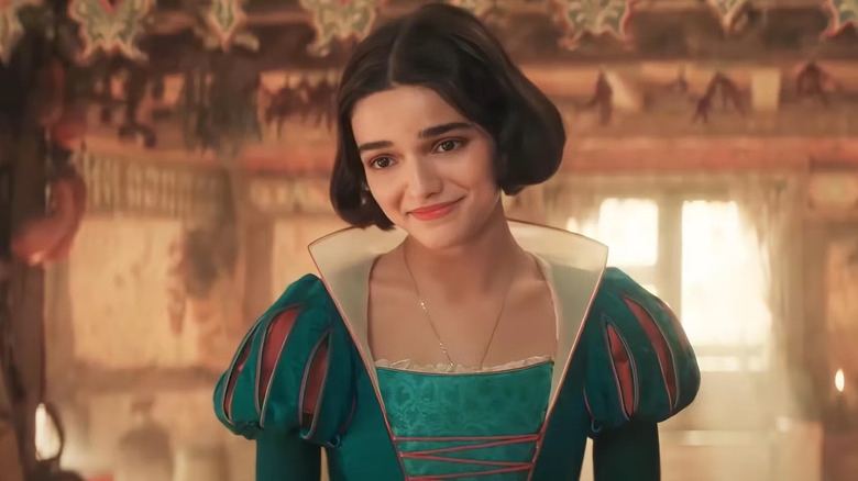 Snow White, wearing her teal dress, smiles warmly with a sunlit window behind her, inside the dwarfs' cottage in Snow White and the Seven Dwarfs