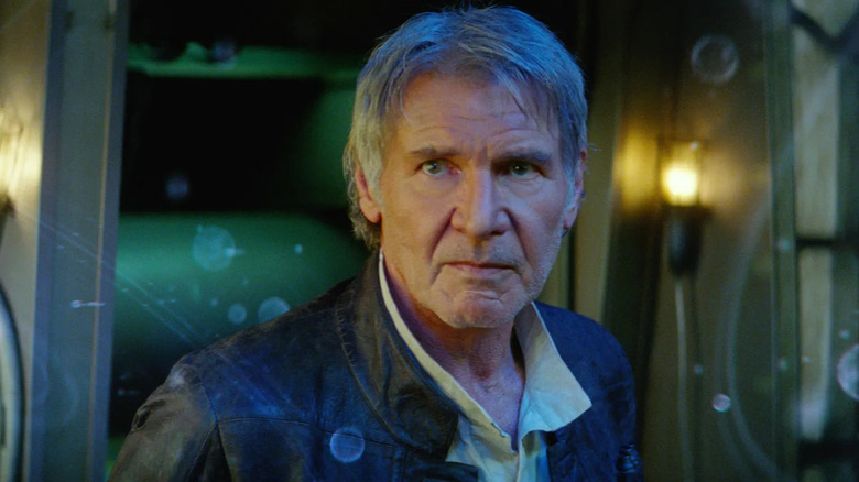 Han Solo looks gravely concerned while wearing a leather jacket and standing in front of a hologram of planets in Star Wars: Episode VII - The Force Awakens