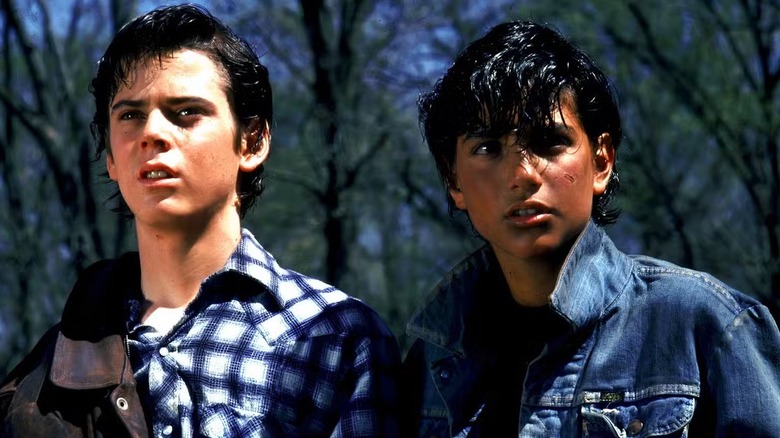 C. Thomas Howell as Ponyboy Curtis and Ralph Macchio as Johnny Cade stand by trees sporting dyed black hair in The Outsiders